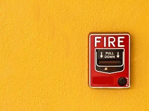 A bright yellow wall with a red fire alarm on it.
