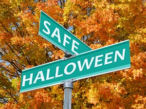 Street signs that say Safe Halloween against a backdrop of fall leaves on trees.