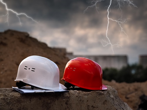 Two hard hats on a construction site with lightning seen in the background.