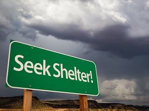 A green sign against a dark stormy sky that says, "Seek Shelter!"