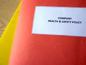 A red folder on a desk with a label on it that says, "Company Health and Safety Policy."