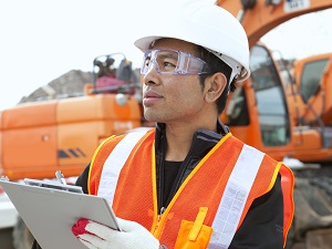An inspector wearing personal protective equipment on a construction site holding a clipboard.