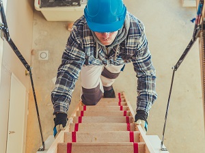 Worker wearing a hard hat climbing up a ladder to get into an attic.