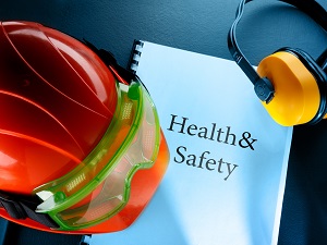 A notebook that says Health and Safety on it surrounded by worker equipment like a hardhat and hearing protection.