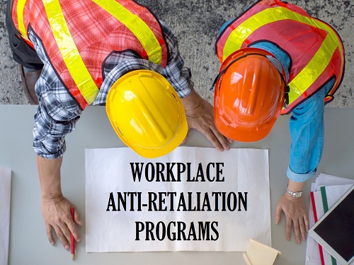 Two workers in hardhats leaning over a table with a sign that says Workplace Anti-Retaliation Programs.