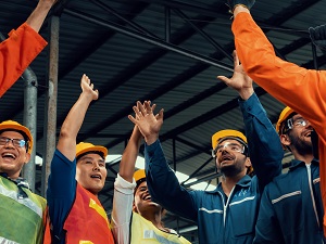 Industrial workers wearing hard hats with their hands in the air looking joyful and excited.