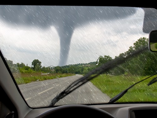 A view of a tornado in the distance as seen from someone sitting in a vehicle.