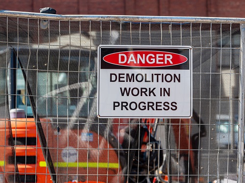 A danger sign on a fence outside a demolition project that says, "Danger, Demolition Work in Progress."