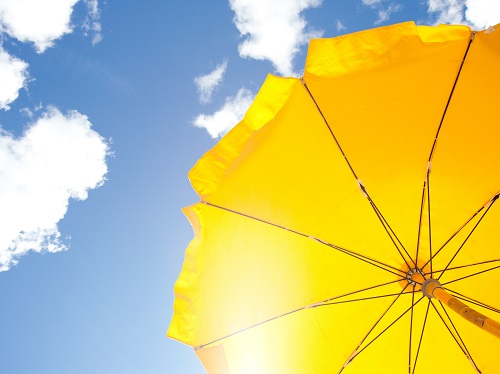 Yellow sun umbrella against a sunny blue sky with fluffy clouds.