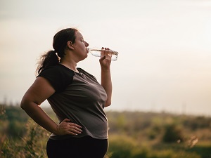 A woman taking a break to drink water during outdoor exercise.