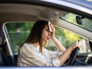 A woman in her car with the windows rolled down feeling very hot.