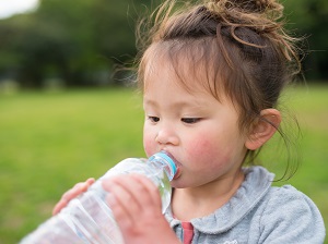 A young child who appears to be hot and sweaty drinking from a water bottle.