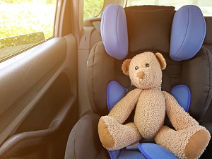 A teddy bear in the car seat of a child in a car.