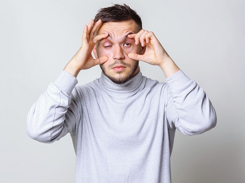 A tired person trying to physically hold their eyelids open dramatically showing that they are exhausted.
