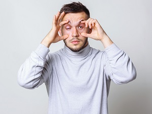 A tired person trying to physically hold their eyelids open dramatically showing that they are exhausted.