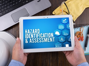 Worker holding a digital table that says Hazard Identification and Assessment.