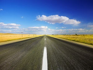 A long stretch of highway and a blue sky with clouds.