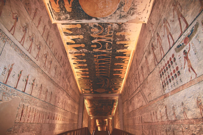 Illuminated stairway inside tunnel of Egyptian pyramid with hieroglyphics along walls and ceiling