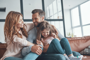 young family of three hugging on couch smiling