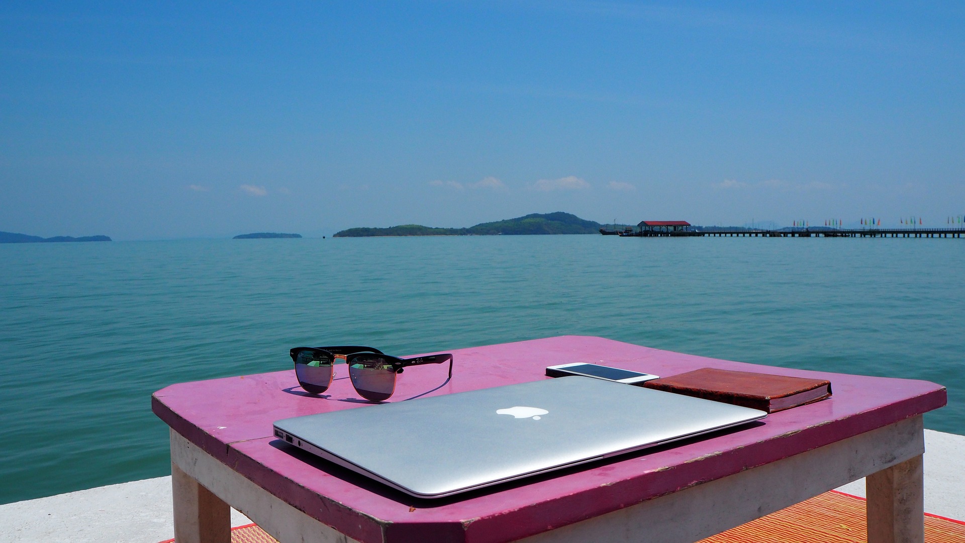 A work setup with a laptop, mobile phone and diary overlooking the ocean