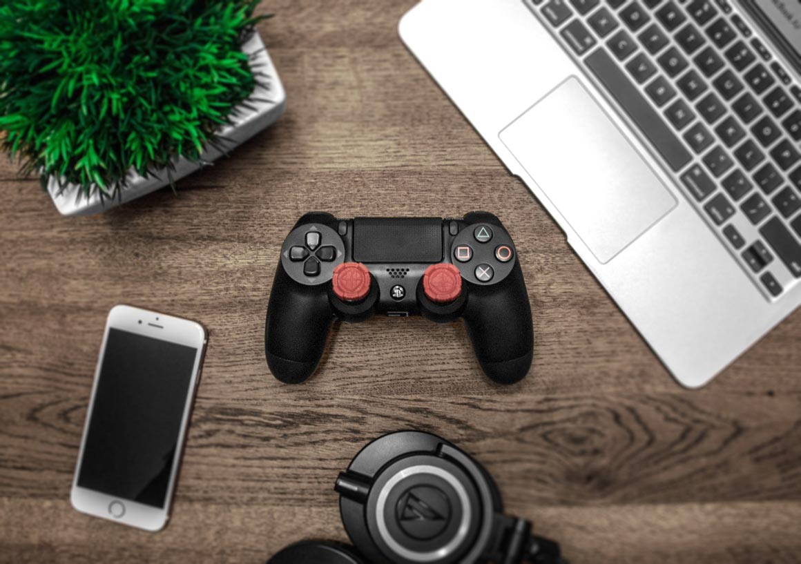 A playstation controller, iPhone, MacBook on a wooden table.