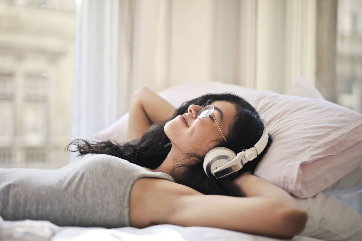 A woman wearing headphones in her bed.