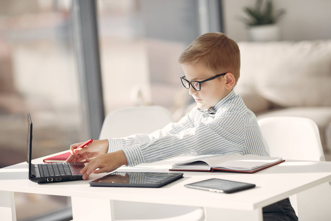 A little boy wearing smart clothes using his dad's computer.