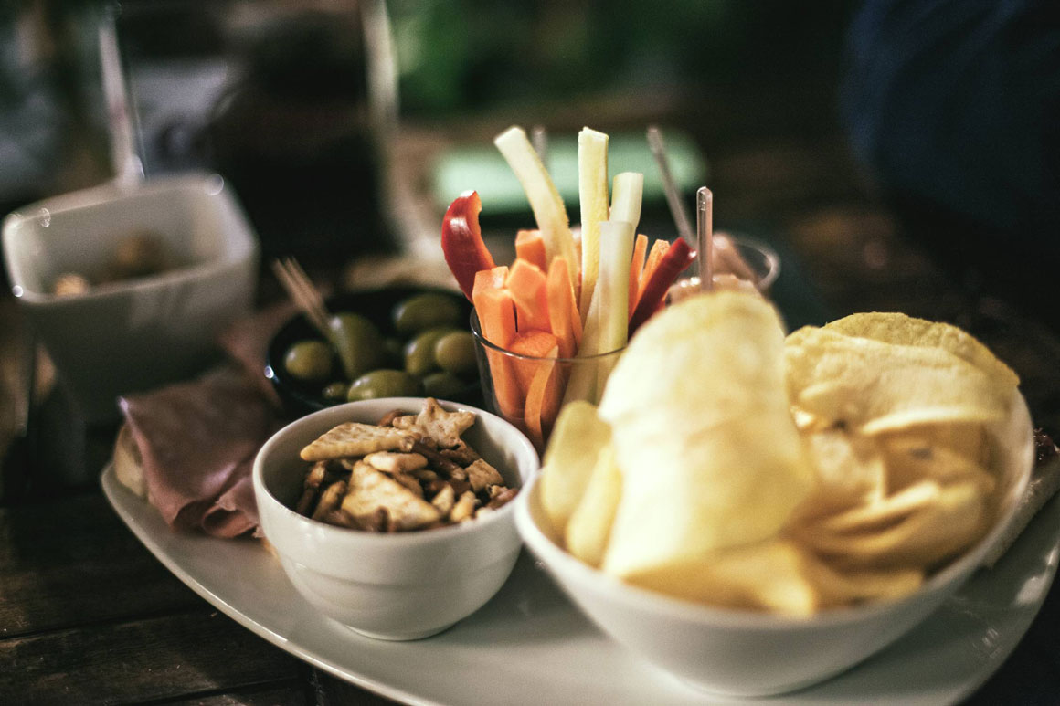 A tray of veggie sticks, olives, chips and crackers.