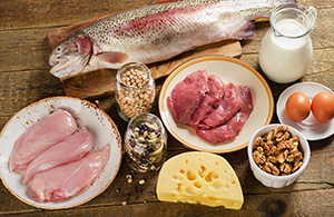 various food items on a table: chicken breast, salmon, milk, nuts, eggs, cheese