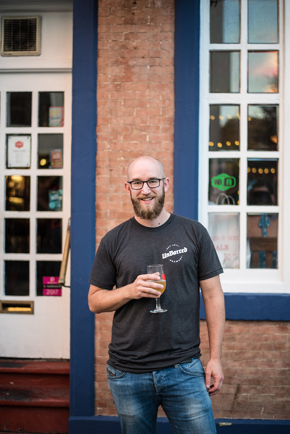 Jordan from Unbarred Brewery poses for a photo outside a pub. He is holding a glass of beer