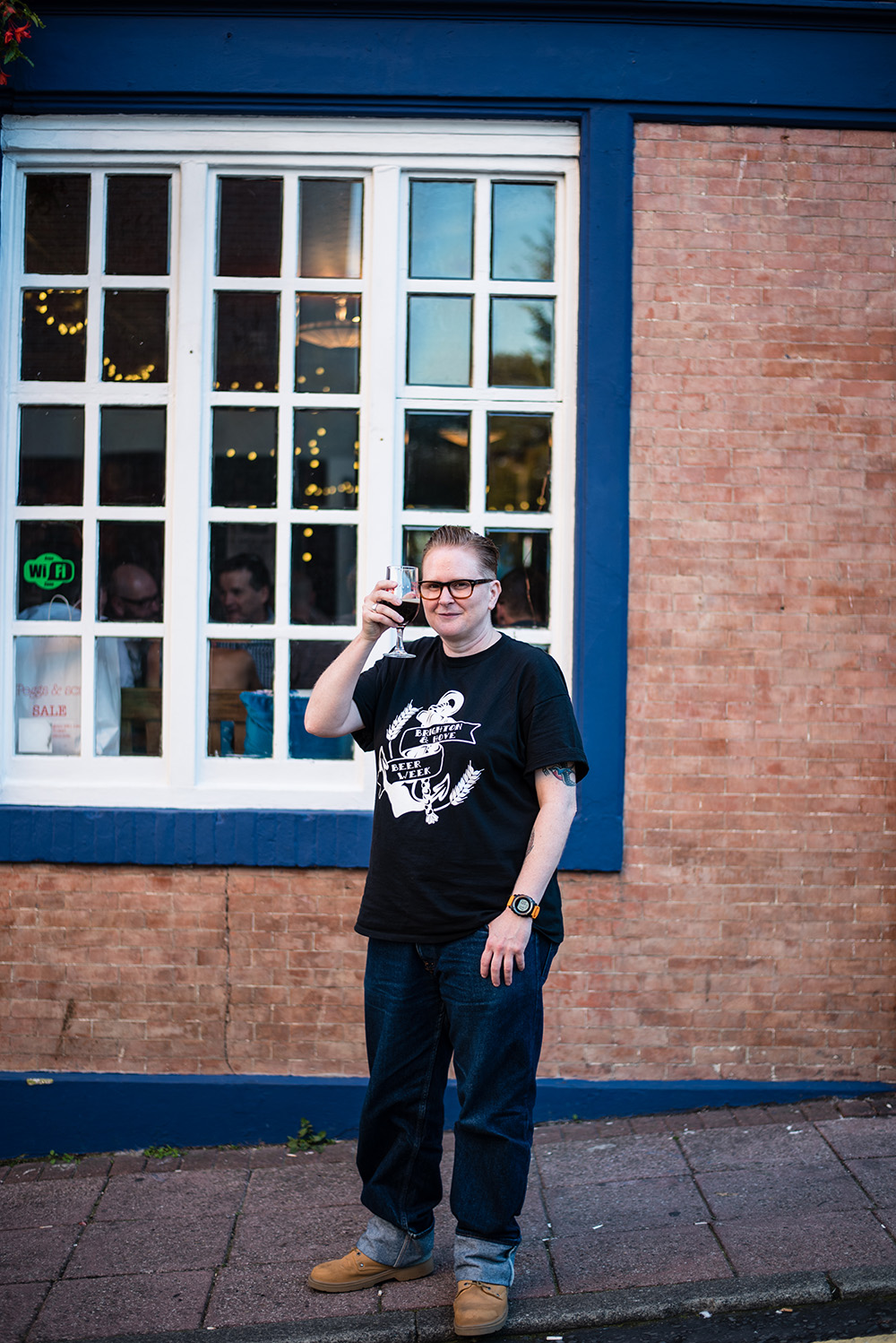 Emma Inch poses for a photo outside a pub. She is raising her glass in the air as a cheers gesture.