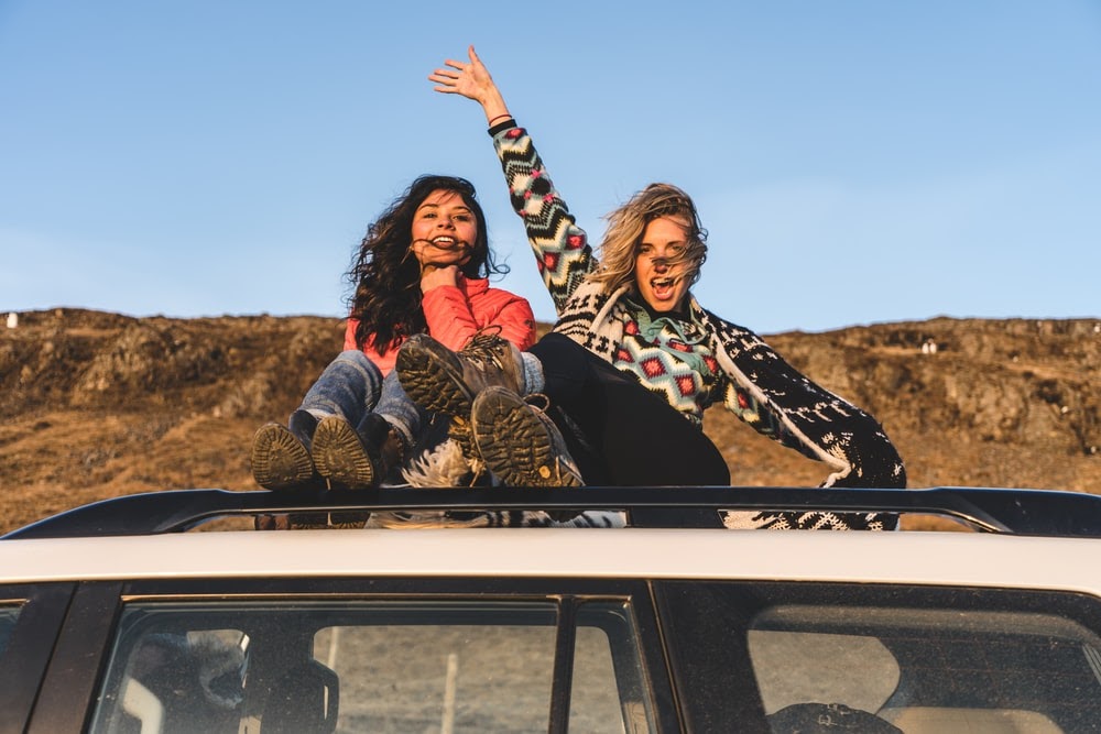 two woman sitting on top of white vehicle under blue sky during daytime