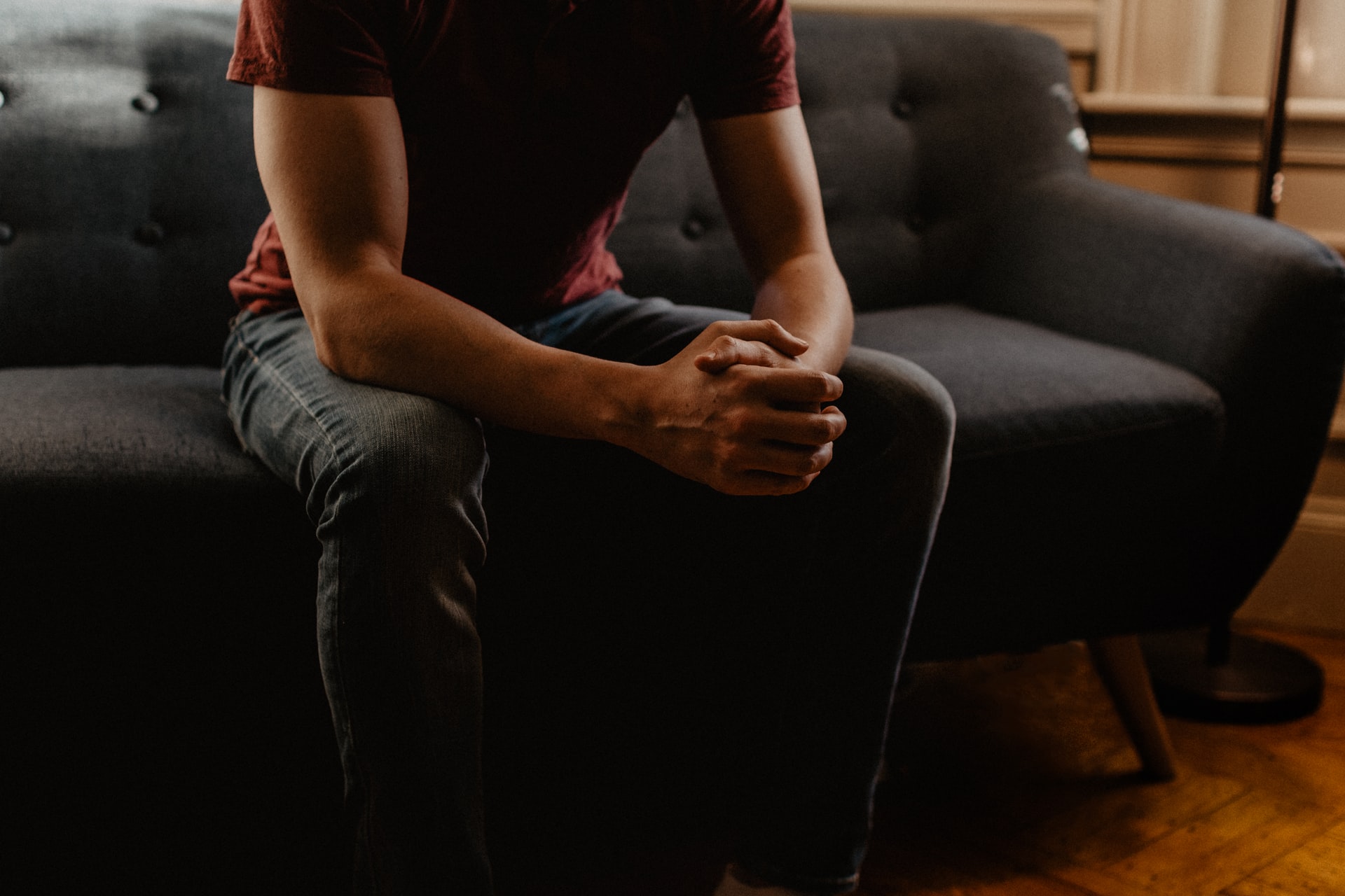 Student struggling with mental health sits on couch with hands clasped together.