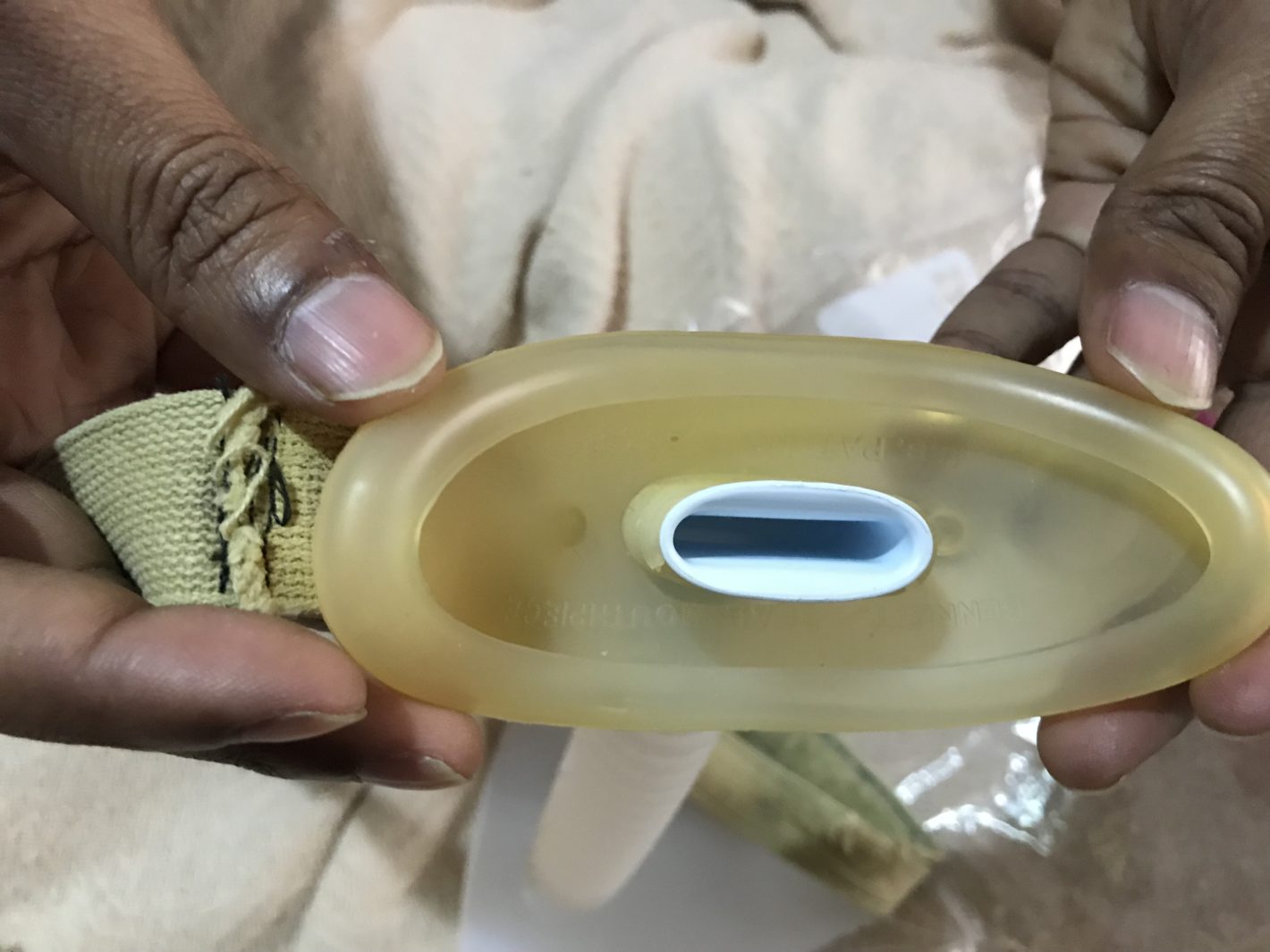 Marilyn's Lip Seal Mask is being held to show what it looks like. It is an oval shaped yellow silicone material with a mouth piece in the middle that is small to provide oxygen.