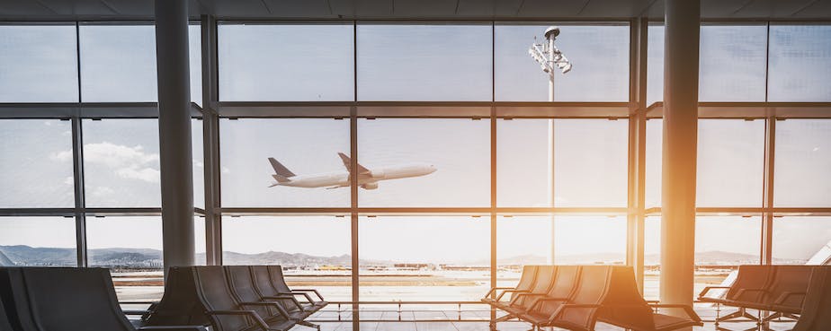 Plane taking off outside window of empty airport seats