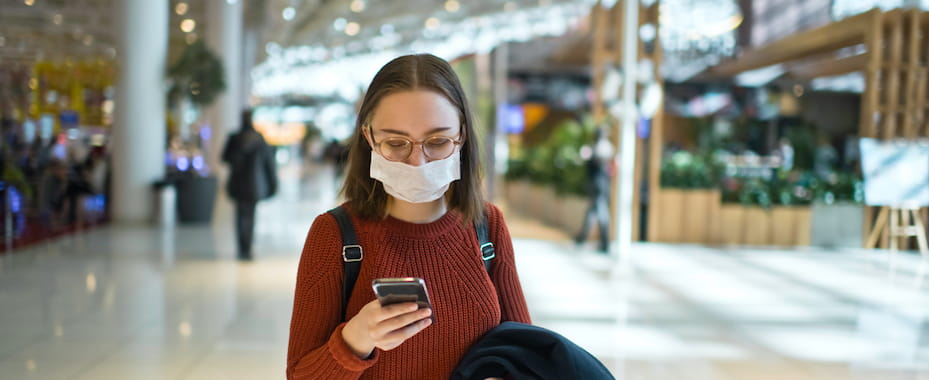 Woman in airport on mobile phone wearing protect face mask during Covid-19