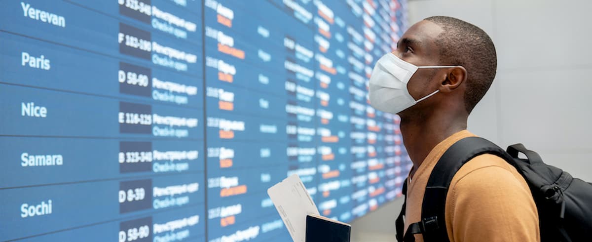 Traveler with facemask at airport checking flight schedules
