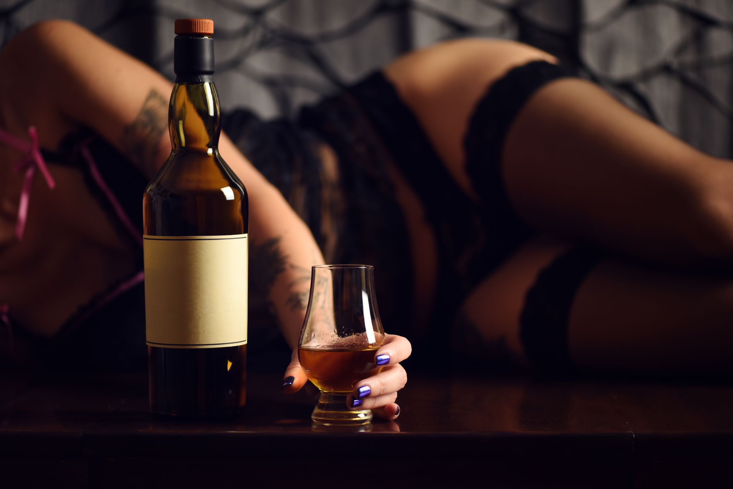 Woman laying on side in lingerie and stockings holding glass with alcohol bottle