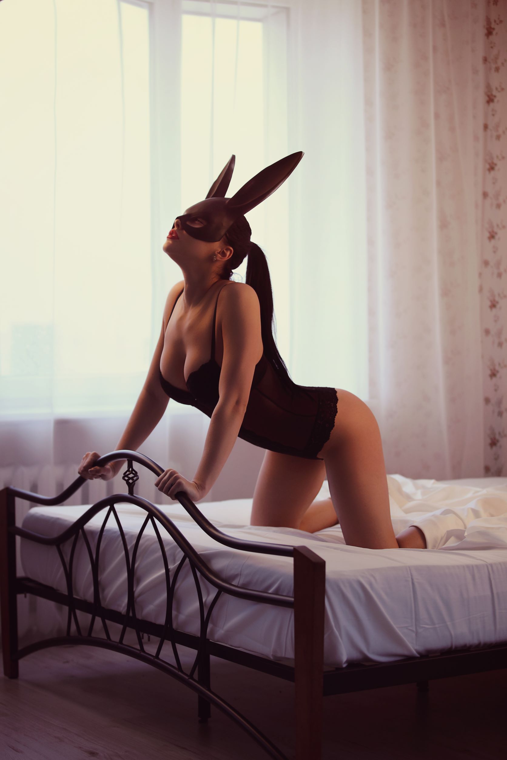 Woman crawling on bed wearing black bodysuit lingerie and black bunny mask