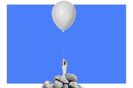Mão segurando balão flutuante acima de uma pilha de pedras, sobre um fundo azul