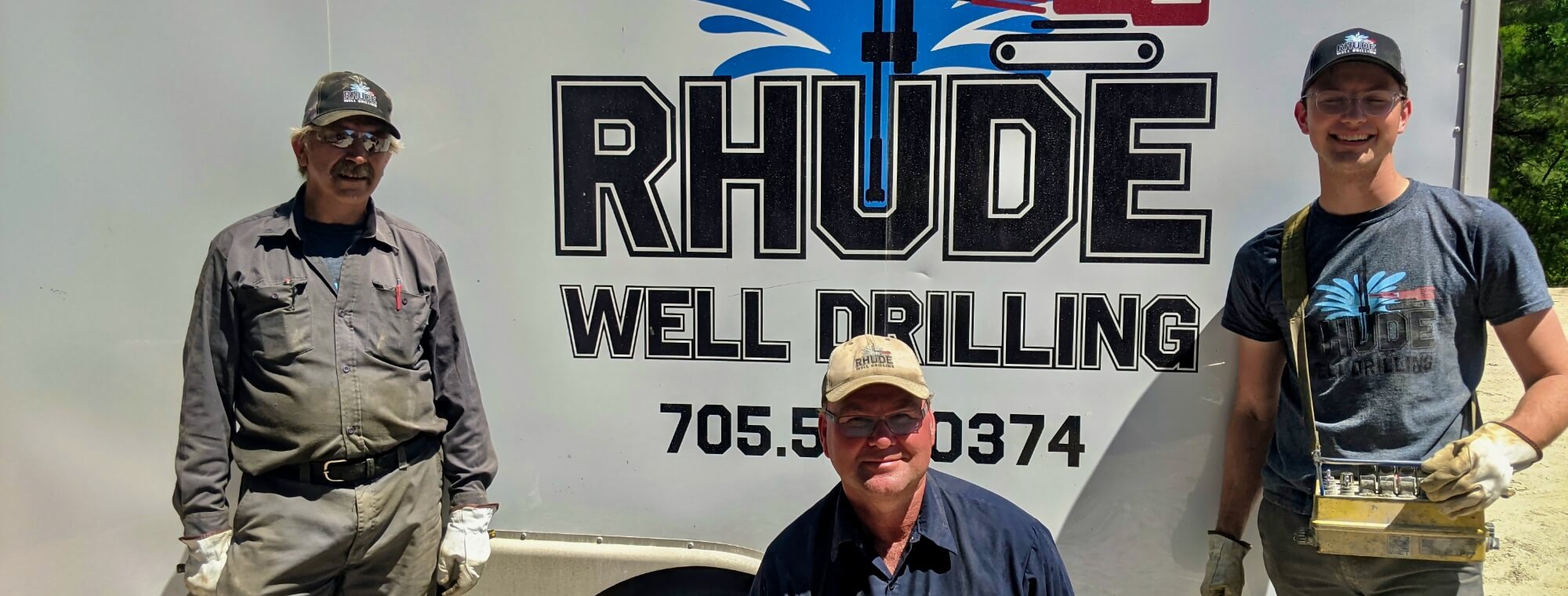 A few of the Rhude Well Drilling technicians smiling in front of a company trailer before starting a job.