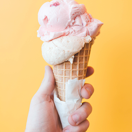 A hand holding a waffle cone with two scoops against a yellow background.