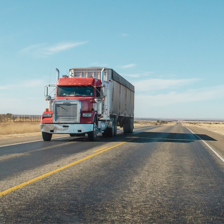 An 18 wheeler with a red cab drives down the interstate in a desert against a clear blue sky.