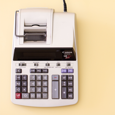 A manual printing calculator sits on a pale yellow background.