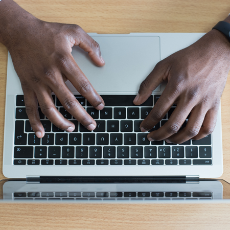 A pair of male hands type on a laptop keyboard.