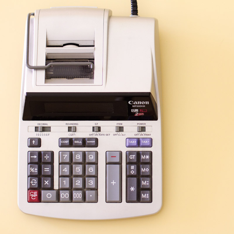 A manual printing calculator sits on a pale yellow background.