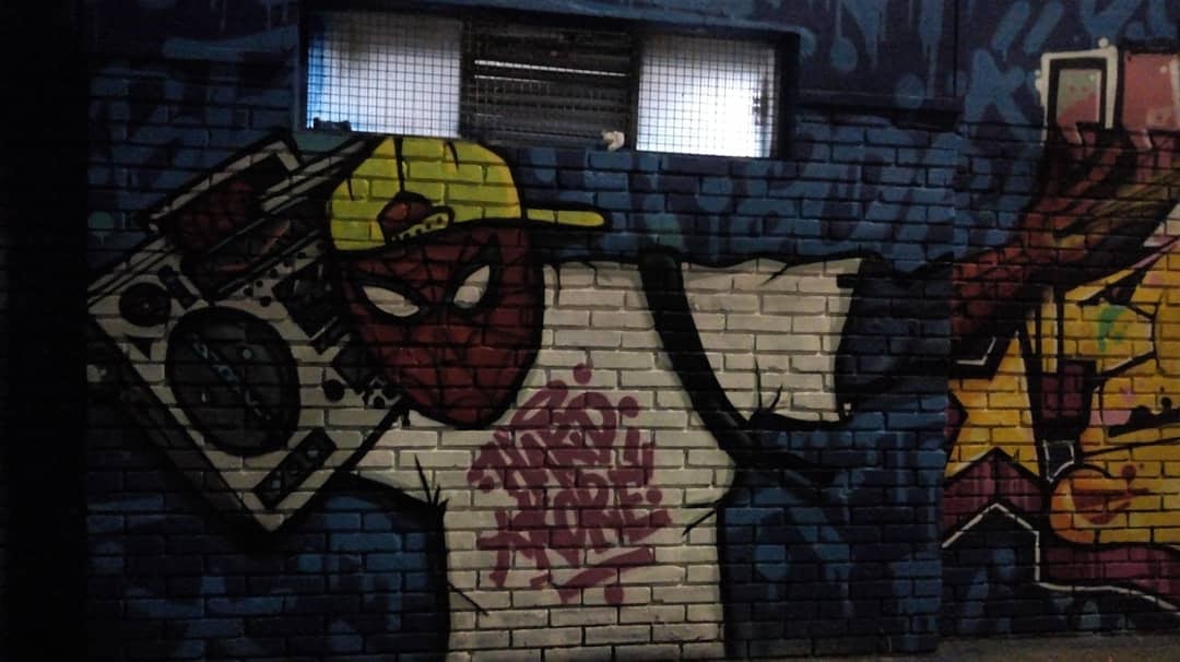 Mural en pared de ladrillo con dibujo de Spider-Man, vistiendo una gorra y con una grabadora en el brazo.