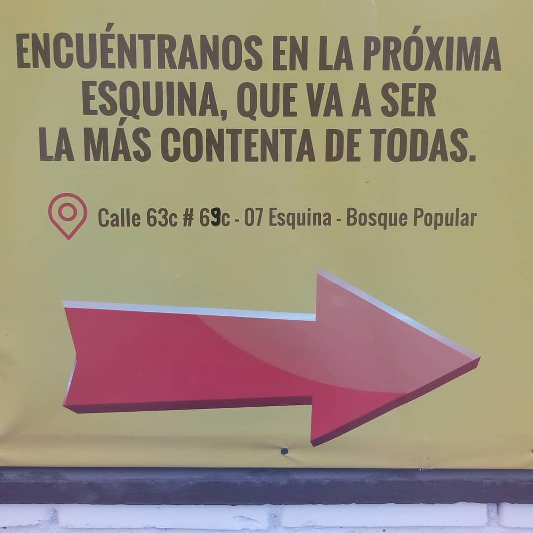 Aviso que dice: Encuéntranos en la próxima esquina, que va a ser la más contenta de todas. Señala una dirección.