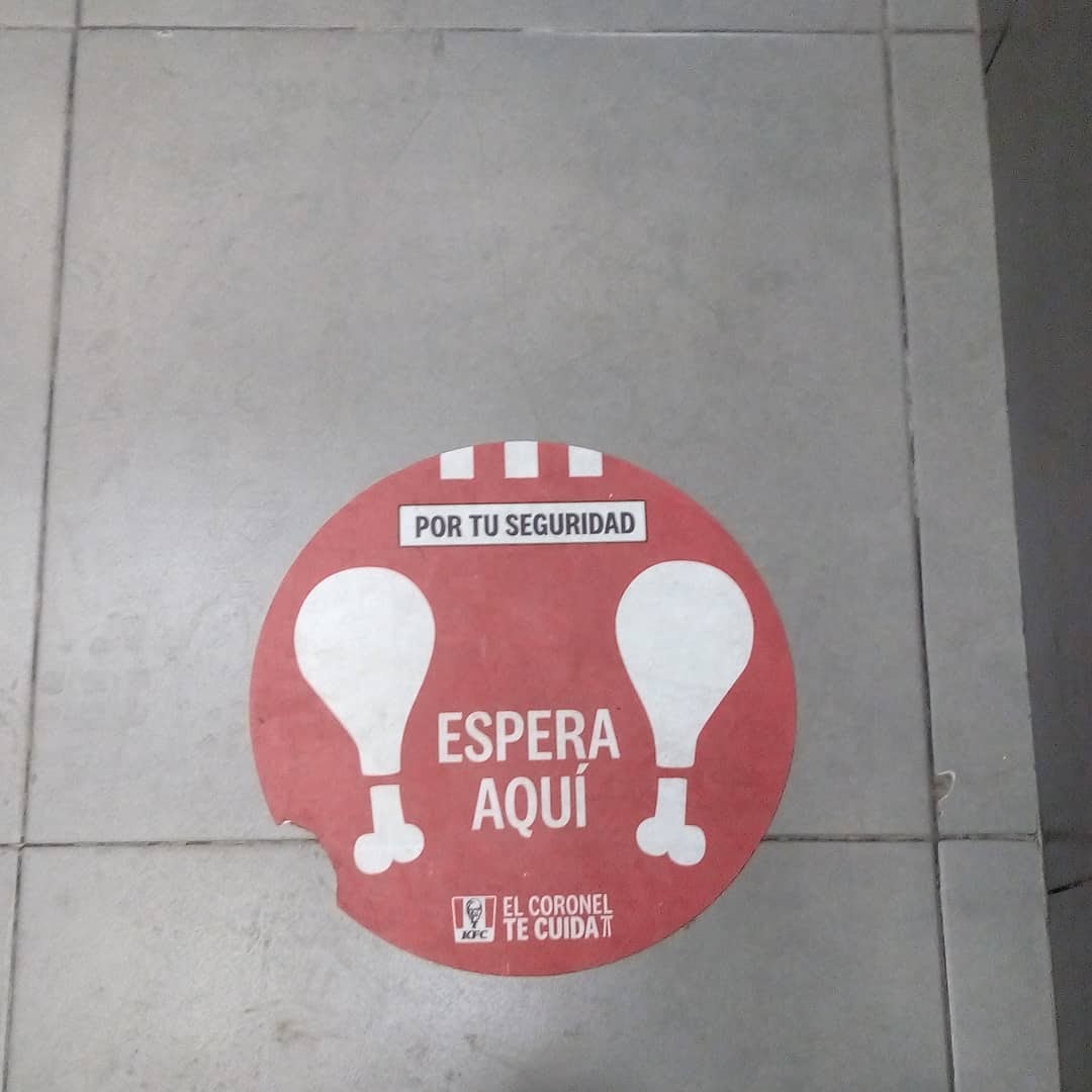 Pegatina o sticker del suelo que dice: Espera aquí. En un emblema de restaurante dice: El coronel te cuida.