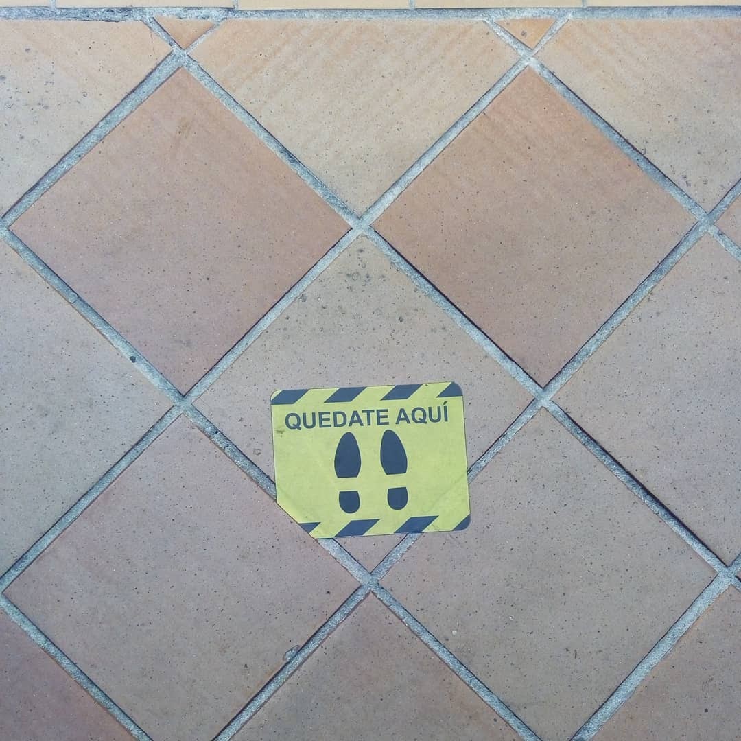 Pegatina o sticker del suelo que tiene huellas y dice: Quédate aquí